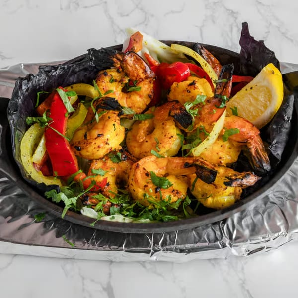 Indian shrimp dish with bell peppers, onions, and cilantro, served with a lemon wedge.