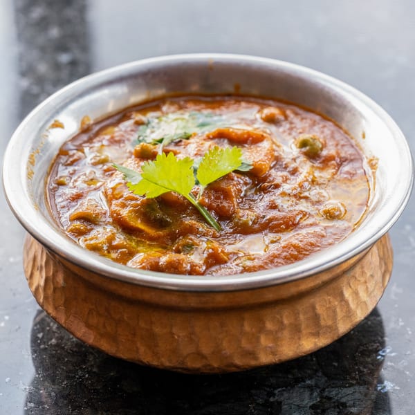 A copper bowl filled with a rich, orange-brown Indian curry, garnished with fresh cilantro.