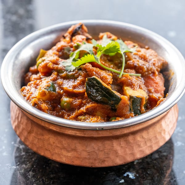 A copper bowl filled with a rich, orange Indian curry, garnished with fresh green cilantro.