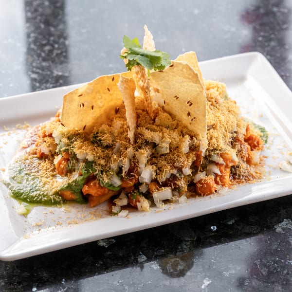 Indian chaat with crispy papadum, sev, chopped onions, and green chutney on a white plate.