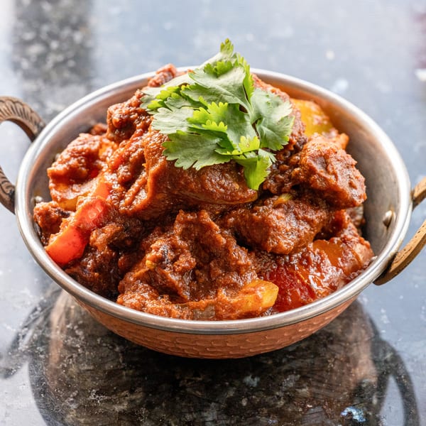 Prabh Indian Kitchen's rich, red curry with meat and vegetables, garnished with fresh cilantro in a copper bowl.