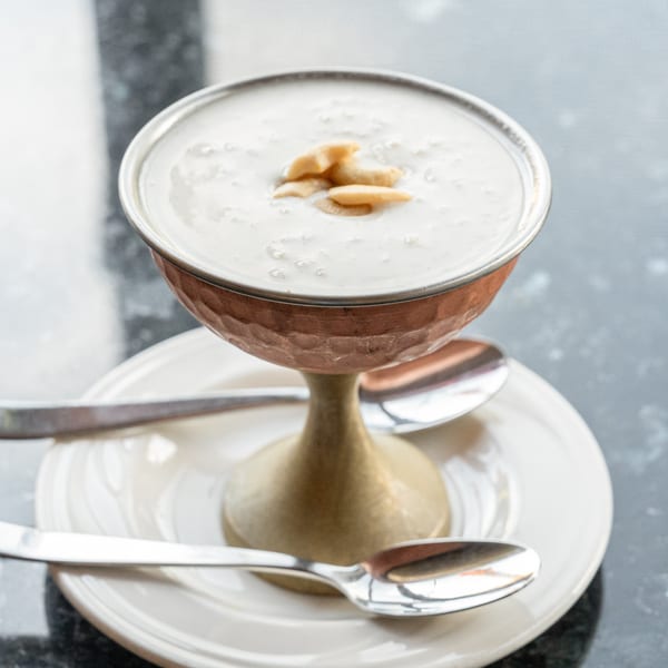 Indian kheer dessert in a copper goblet with cashews, served on a white plate with spoons.
