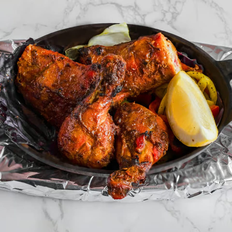 Prabh Indian Kitchen's Tandoori Chicken, with lemon and peppers, served in a black skillet.