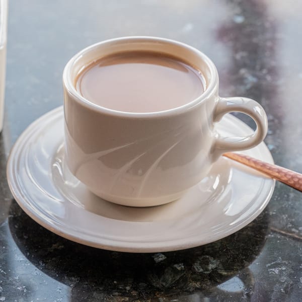 A white cup of Indian chai tea with a spoon on a matching saucer sits on a dark table.